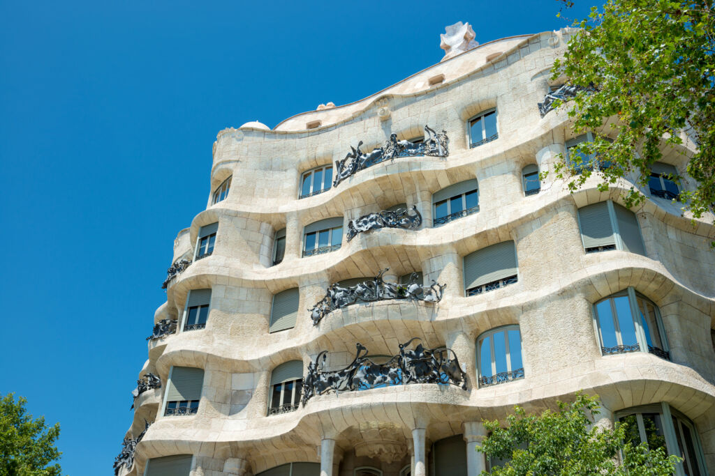 Facade of Casa Mila with green trees on the street of Barcelona, Spain. Famous building designed by Antoni Gaudi, UNESCO list